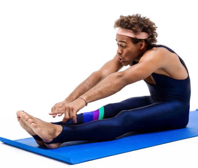 Young handsome sportive african man stretching, sitting on karemat over white background. Copy space.